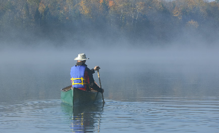photo of a man paddling a canoe on a misty lake