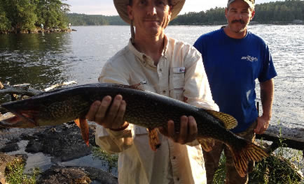 A man standing by the water showing off a fish he caught.